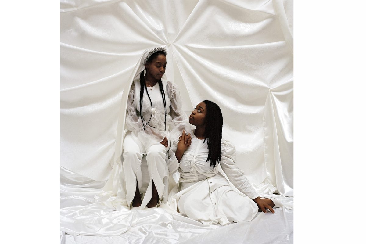 Young twin women sitting in room filled with fabric, holding hands.