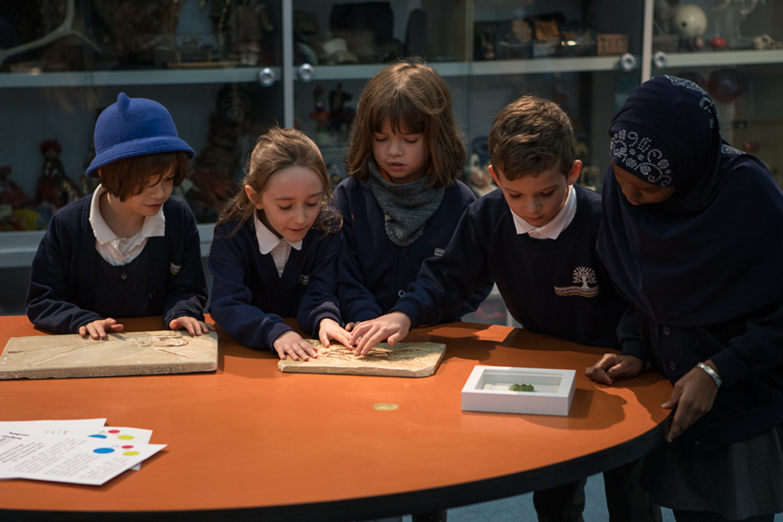 Five school children sit at a table looking at a workbook