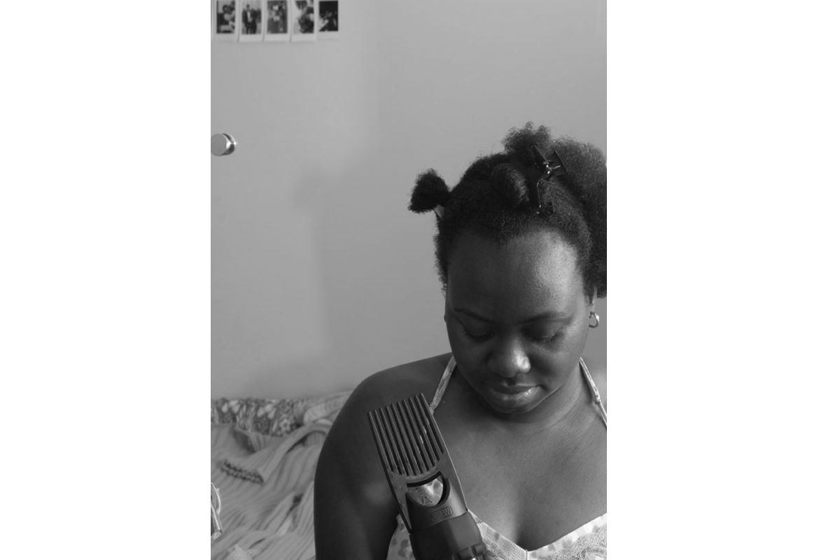 Black and white photo of a Black woman with parts of her hair clipped up, holding some clippers