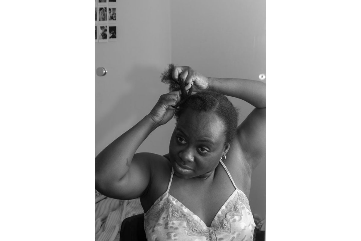 Black and white photo of a Black woman doing her hair in a mirror