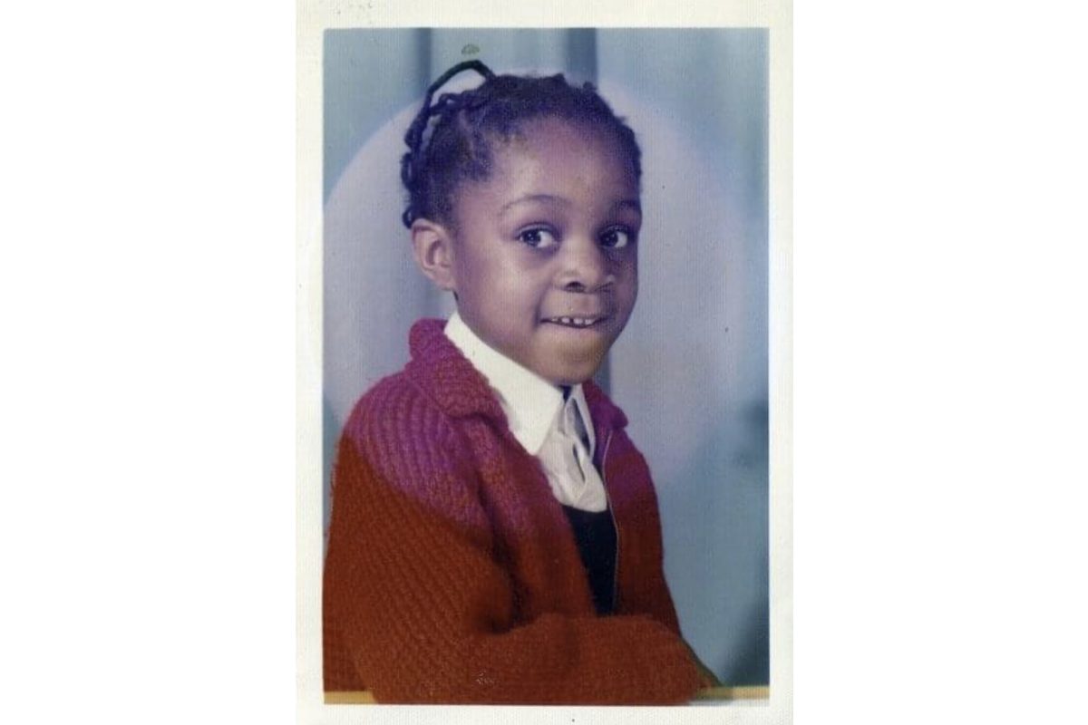 A school photo of a young Black girl, wearing school uniform and looking at the camera with a smile. She has her hair in braids.