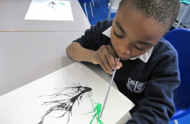 A boy blowing link shapes through a straw with paint