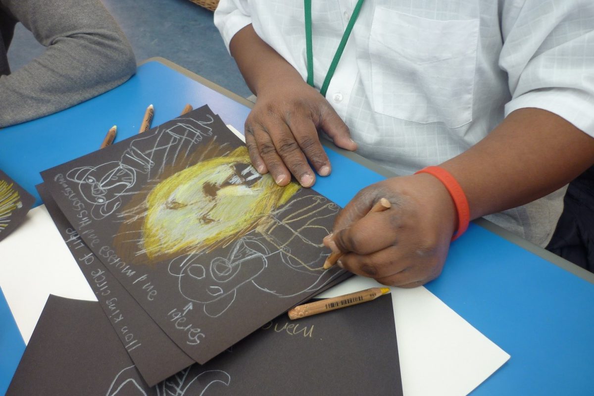 Child's hands holding a drawing of a lion on black paper