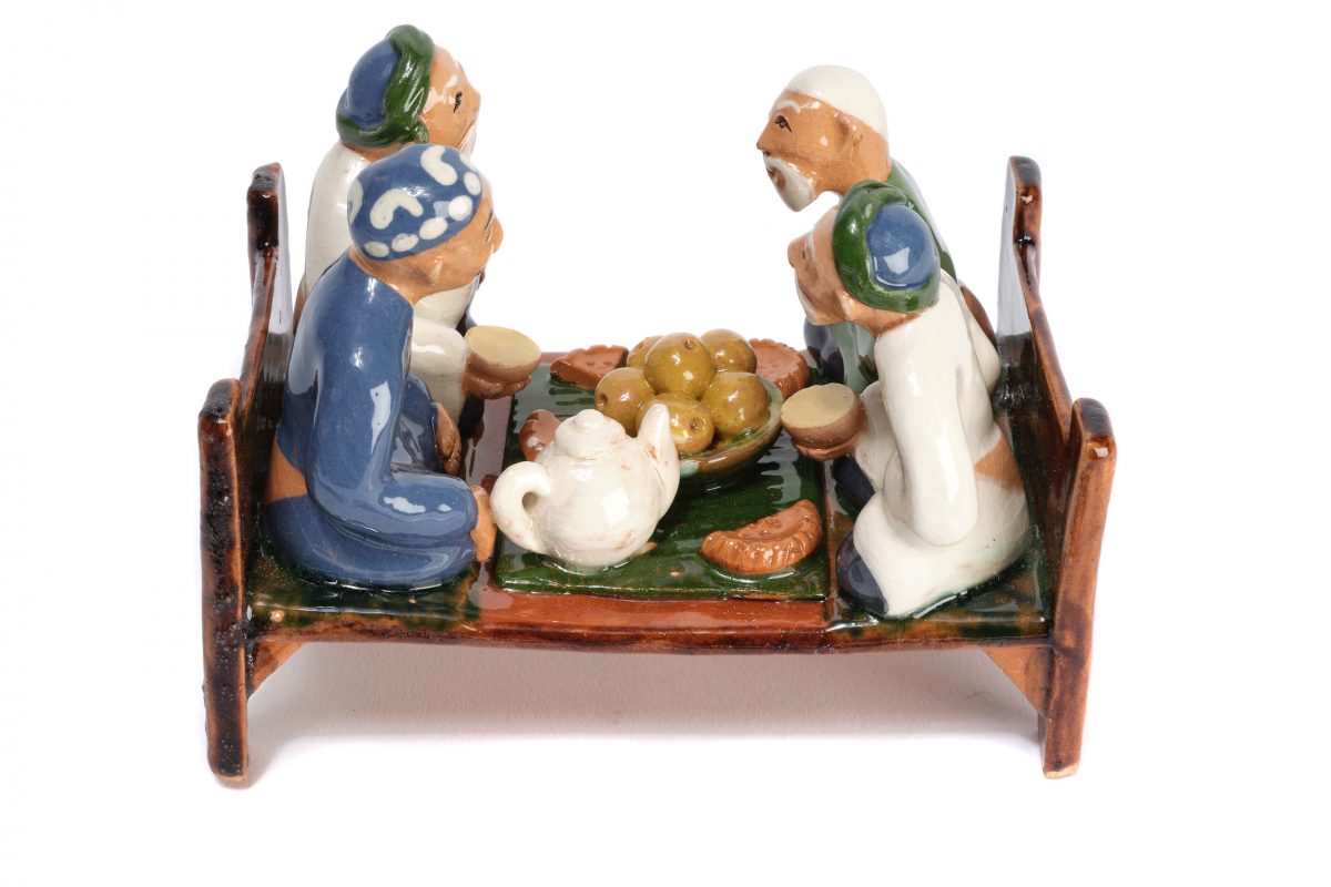 A china model of four men drinking tea and sharing food on a raised platform