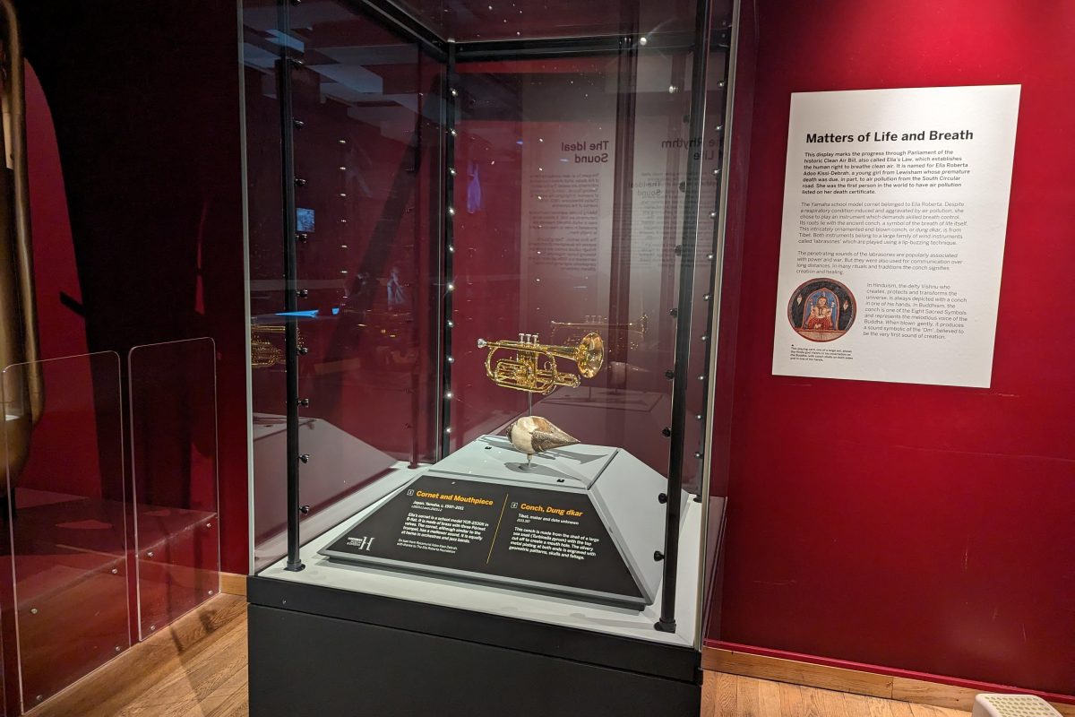 Matters of Life and Breath display case, with a shiny golden cornet and a conch shell inside the case. The front of the case has two labels describing the objects, although these cannot be read from the picture. Next to the display case is a sigh which reads 'Matters of Life and Breath' followed by more text which again cannot be read from the photo.