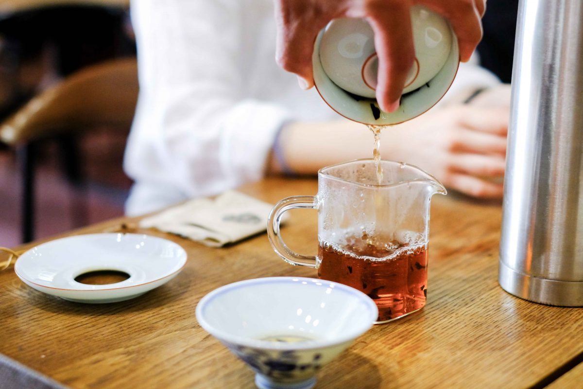A person pours tea into a jug from a teapot