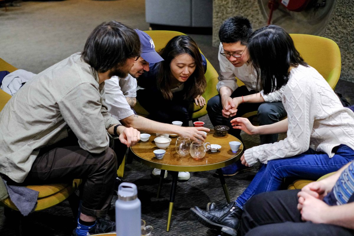A group of people sat together gather around a table with teacups on