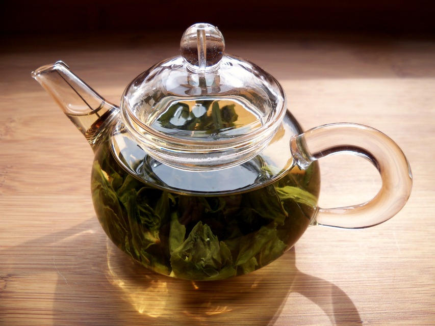 Tea leaves steep in a clear glass teapot