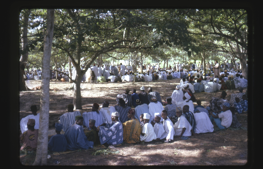A large group of seated people praying outdoors