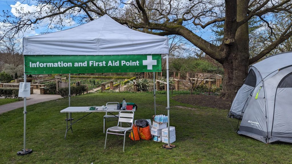 A white gazebo with a banner reading 'information and first aid point' and with a table and chair underneath it