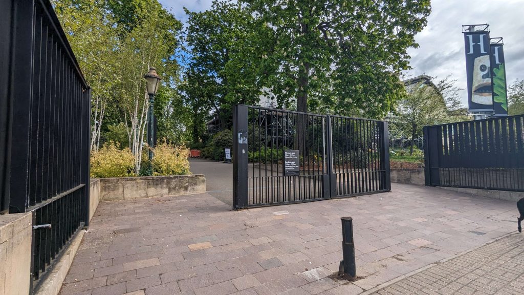 A large black gate in the centre of a wide path, with gaps on either side to enter