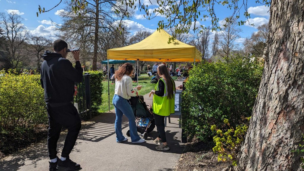 A yellow gazebo surrounded by bushes with a person in his-vis standing in front of it