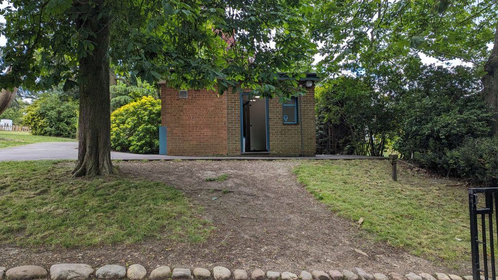 A small building amongst the Gardens and slightly blocked from view by a tree branch. 